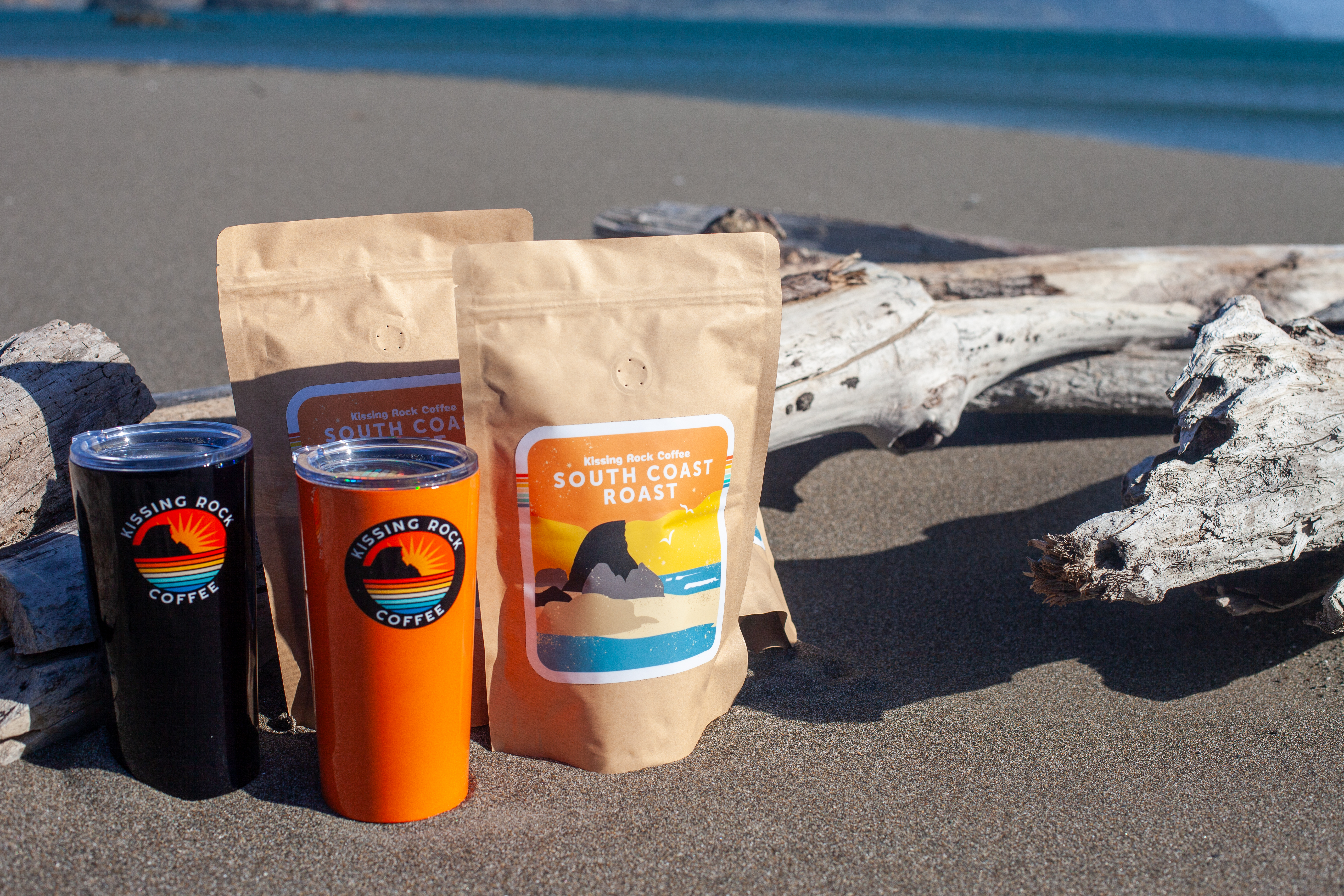 Kissing Rock Coffee products on driftwood at the beach