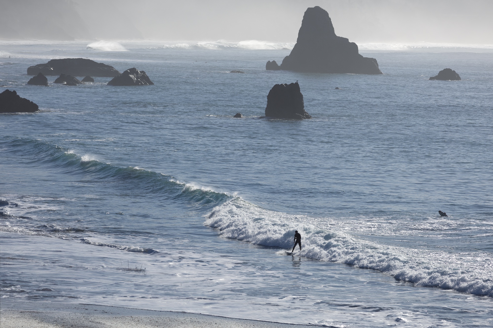 Surfer riding a wave with sea stacks in the background at Port Orford